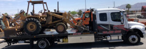 Economy Towing transporting a backhoe secured on a flatbed